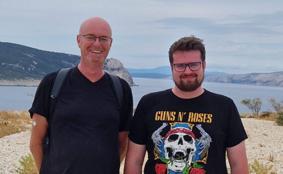 Hans Schwarzmann und Quirin Schwarzmann stehen nebeneinander. Vor einem Meer. Berge im Hintergrund