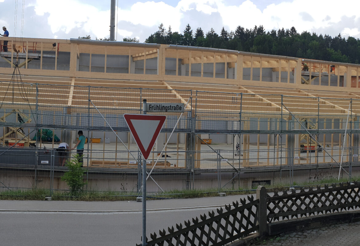 Ein Bild der Lagerhalle. Die Lagerhalle wird gerade gebaut Bauarbeiter stehen auf und unter Dem Hölzernen Umriss der Halle.